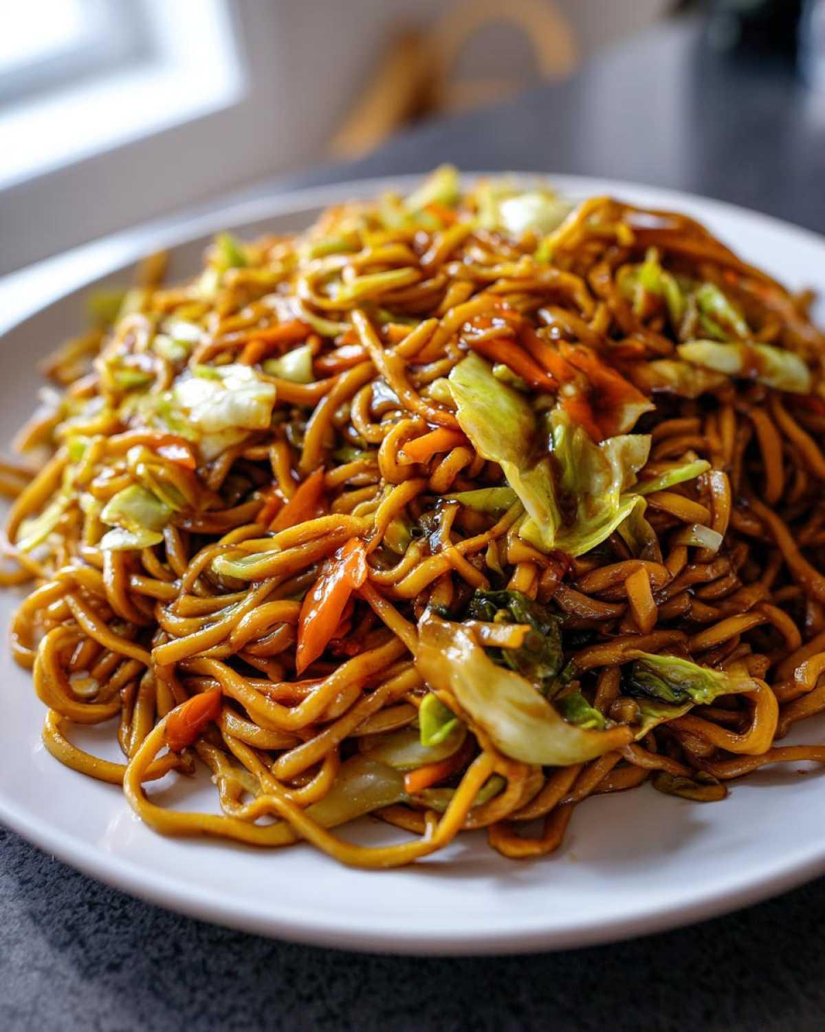 A close-up shot of freshly prepared fried noodles mixed with cabbage and carrots on a white plate.