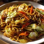 A close-up of a bowl filled with savory, glossy fried noodles mixed with stir-fried cabbage and carrots.