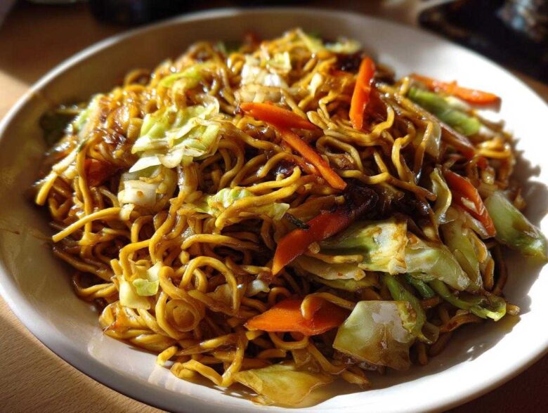 A close-up of a bowl filled with savory, glossy fried noodles mixed with stir-fried cabbage and carrots.