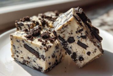 Two rich squares of white chocolate Oreo fudge studded with dark cookie pieces, sitting on a white plate.