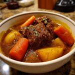 Close-up of a rich, dark brown pork stew featuring tender meat chunks, bright orange carrots, and yellow potatoes.