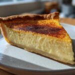 A close-up slice of amazing custard pie with a creamy yellow filling and a beautifully caramelized, slightly burnt sugar top.
