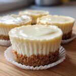 Four perfectly formed mini cheesecake desserts with graham cracker crusts sitting on a wooden board.