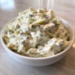 Close-up of a generous serving of creamy pickle dip mixed with chopped pickles and dill in a white bowl.