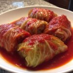 Close-up of five savory Stuffed Cabbage Rolls simmering in a vibrant red tomato sauce in a white bowl.