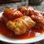 Four servings of amazing Stuffed Cabbage Rolls simmered in a rich, red tomato sauce on a white plate.