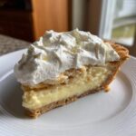 A thick slice of banana cream pie recipe showing creamy filling, crust, and a generous topping of whipped cream.