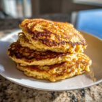 A close-up stack of three golden-brown banana oatmeal pancakes on a white plate.