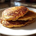 A stack of three golden-brown banana oatmeal pancakes resting on a white plate.
