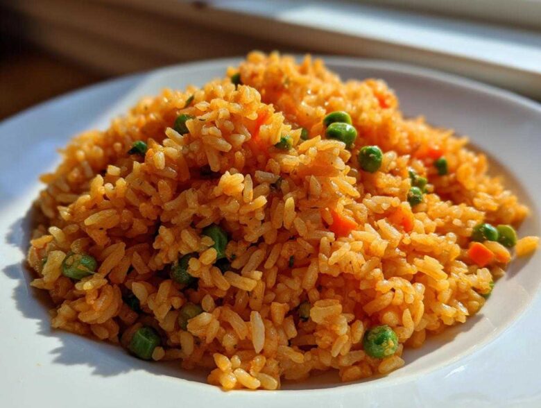 A close-up of fluffy, bright orange Spanish rice mixed with green peas and diced carrots served on a white plate.