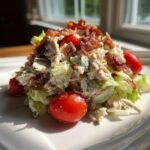 A mound of creamy blt chicken salad mixed with lettuce, topped with crispy bacon bits and cherry tomatoes.