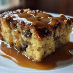 A close-up of a moist slice of bread pudding with bourbon sauce generously drizzled over the top.