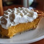 A close-up slice of rich, orange butterscotch pie topped generously with piped whipped cream.