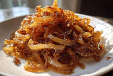 Close-up of a mound of deeply browned and glossy caramelized onions served on a white plate.