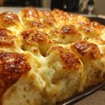 Close-up of baked Hawaiian roll garlic bread with melted, golden-brown cheese bubbling between the rolls.
