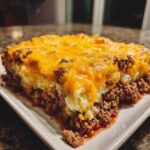 A generous slice of meatloaf casserole featuring a ground beef base, mashed potatoes, and melted cheddar cheese topping.
