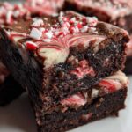 Two stacked, fudgy candy cane brownies featuring a peppermint swirl topping and crushed candy cane pieces.