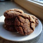 A stack of chewy gingersnap cookies coated in sparkling sugar crystals, resting on a white plate.
