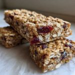 Two stacked, chewy homemade granola bars made with oats and dried cranberries, sitting on a light surface.
