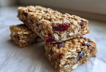 Two stacked, chewy homemade granola bars made with oats and dried cranberries, sitting on a light surface.