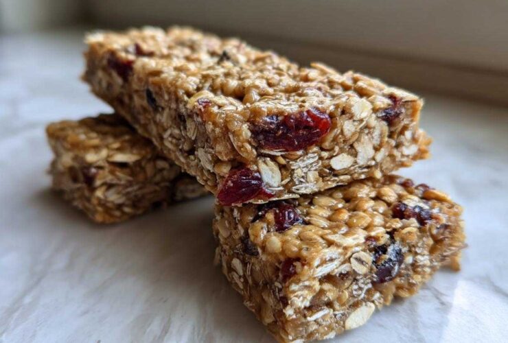 Two stacked, chewy homemade granola bars made with oats and dried cranberries, sitting on a light surface.