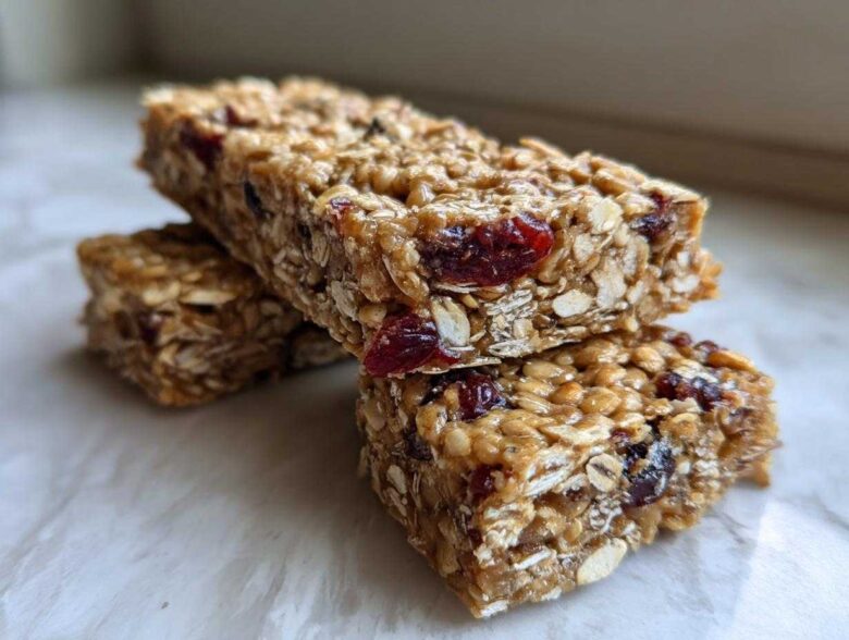 Two stacked, chewy homemade granola bars made with oats and dried cranberries, sitting on a light surface.