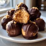 A stack of chocolate-covered peanut butter balls, one bitten open to show the creamy filling.