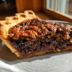 Close-up of a rich, gooey slice of chocolate pecan pie showing the flaky crust and dark filling.
