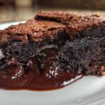 Close-up of a moist slice of chocolate pudding cake oozing rich, dark chocolate sauce onto a white plate.