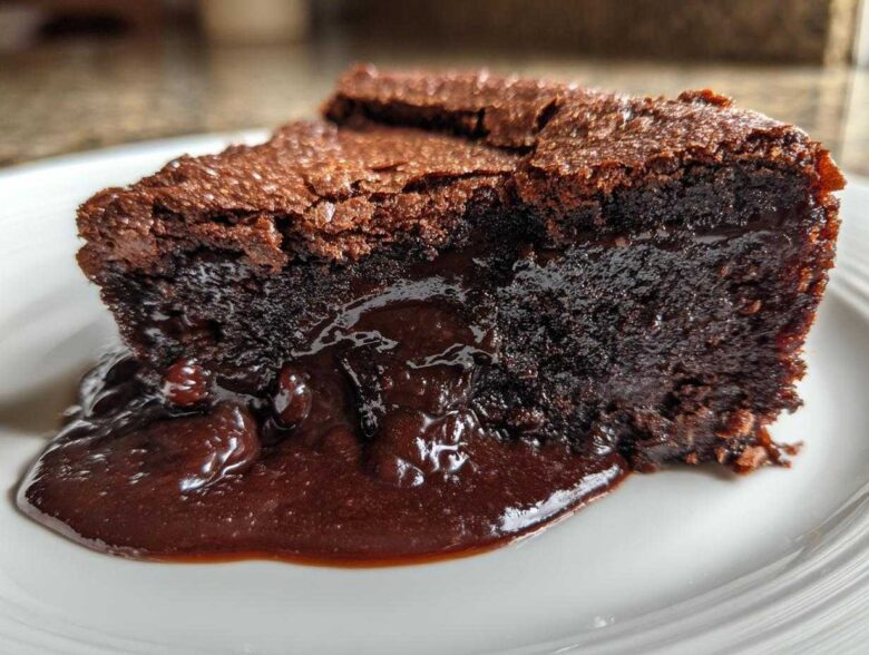 Close-up of a moist slice of chocolate pudding cake oozing rich, dark chocolate sauce onto a white plate.