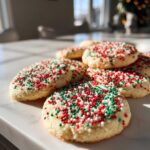 A pile of freshly baked christmas sprinkle sugar cookies topped with red, green, and white nonpareils.