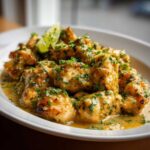 Close-up of tender pieces of coconut lime chicken coated in a creamy sauce and topped with fresh parsley and a lime wedge.