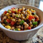 Close-up of vibrant cowboy caviar salad featuring black-eyed peas, corn, and diced peppers in a white bowl.