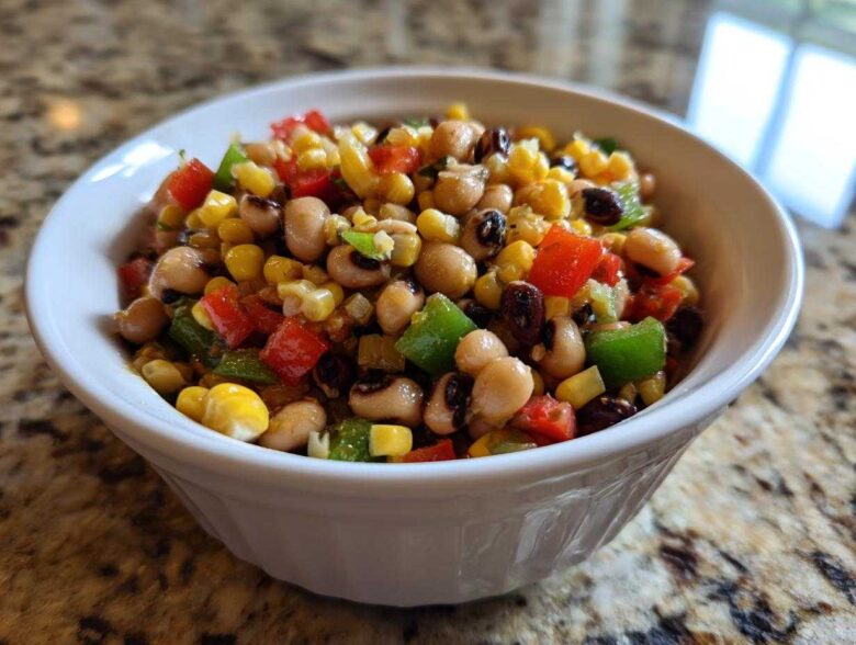 Close-up of vibrant cowboy caviar salad featuring black-eyed peas, corn, and diced peppers in a white bowl.