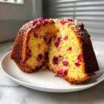 Close-up of a cranberry orange cake cut in half, showing bright cranberries in the yellow crumb.