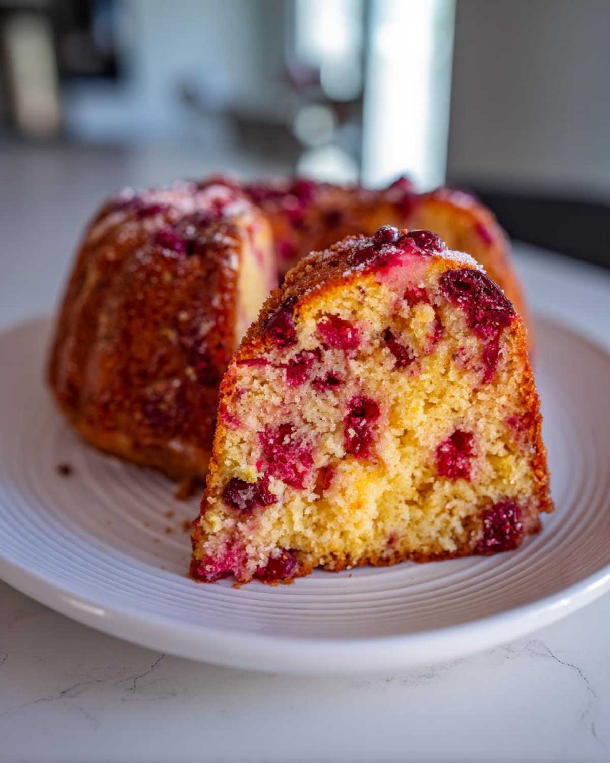 Close-up of a slice of moist cranberry orange cake showing bright red cranberries baked into the yellow crumb.
