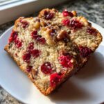 Two close-up slices of moist cranberry walnut bread showing bright red cranberries and walnuts.