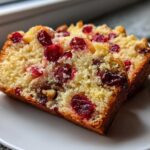 Two thick slices of moist cranberry walnut bread, studded with bright red cranberries and walnuts, resting on a white plate.
