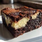 A close-up of a fudgy cream cheese brownies slice showing the dark chocolate base and creamy white swirl.