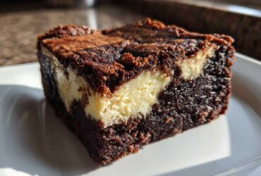 A close-up of a fudgy cream cheese brownies slice showing the dark chocolate base and creamy white swirl.