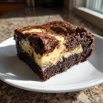 A rich, fudgy square of cream cheese brownies with a visible cheesecake swirl on a white plate.
