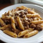 Close-up of a white bowl filled with creamy beef pasta made with penne noodles and ground beef sauce.