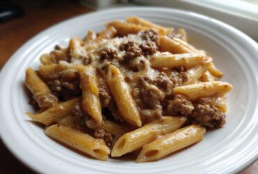 Close-up of a white bowl filled with creamy beef pasta made with penne noodles and ground beef sauce.