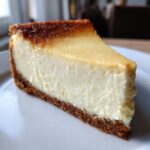 A perfect slice of creamy cheesecake recipe with a thick graham cracker crust and a slightly browned top.