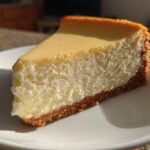 A perfect slice of creamy cheesecake recipe on a white plate, showing a thick graham cracker crust.