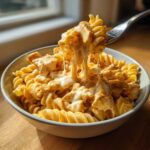 A fork lifting a bite of creamy cheesy chicken pasta, showing long, delicious cheese pulls.