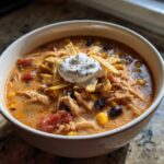 Close-up of a creamy chicken tortilla soup topped with sour cream, tortilla strips, corn, and black beans.
