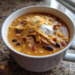 A close-up of a creamy bowl of chicken tortilla soup topped with sour cream and tortilla strips.