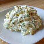 A mound of creamy cucumber salad mixed with dill, resembling a thick pickle dip texture.