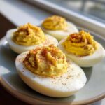 Four creamy deviled eggs, piped high with yolk filling and sprinkled with paprika, sitting on a light plate.